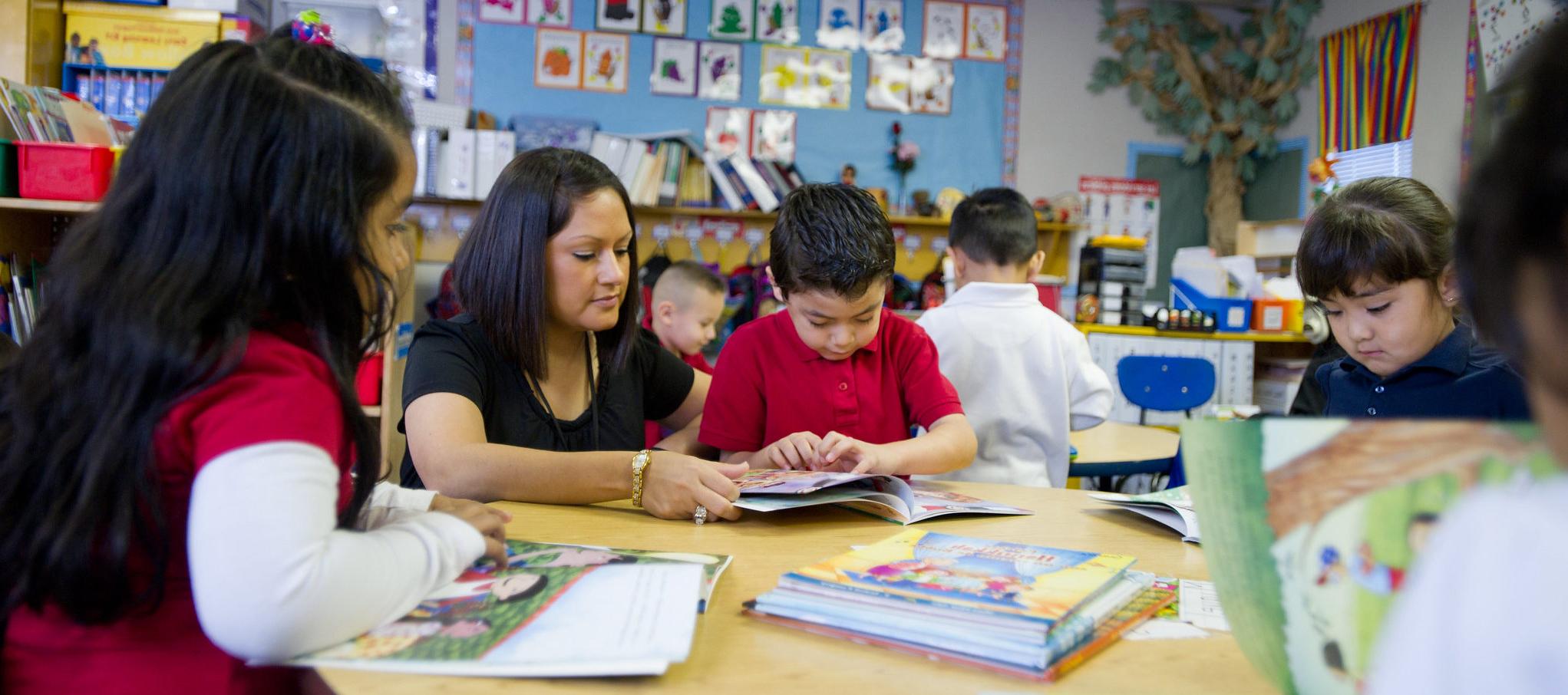 hispanic female teacher help young hispanic boy in classroom.