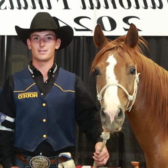 A person in western attire poses for a photo next to a horse.